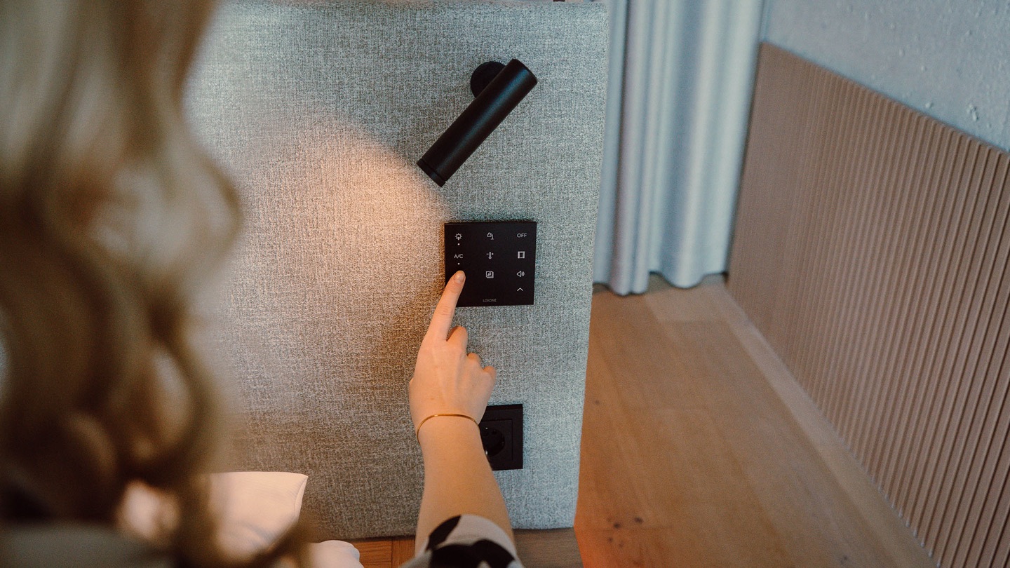 A hand operating an anthracite Loxone Touch Pure Flex beside a reading light